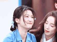 a woman in a blue shirt is smiling while another woman looks on
