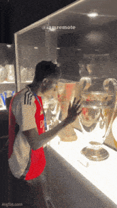 a man in a red and white shirt looks at a trophy in a glass case