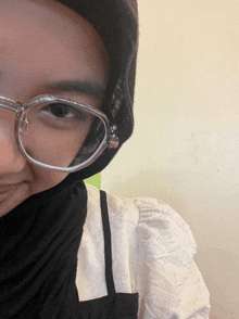 a woman wearing glasses and a black hijab is smiling