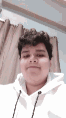 a young man with curly hair is wearing a white hoodie and smiling