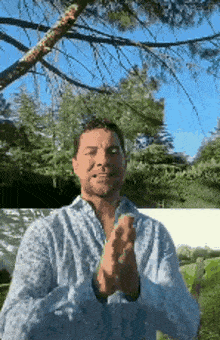 a man wearing a blue shirt is clapping his hands in front of a tree .