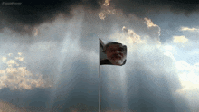 a flag with a man 's face on it is flying in front of a cloudy sky