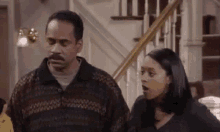 a man and a woman are standing next to each other in a living room in front of a staircase .