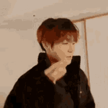 a man in a black jacket is standing in a room with his hand on his neck .