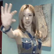 a woman in a denim jacket is waving her hand in front of a map on the wall