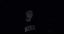 a man wearing a nike shirt is standing in the dark .