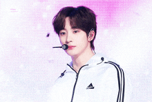 a young man wearing a white adidas jacket is standing in front of a pink background