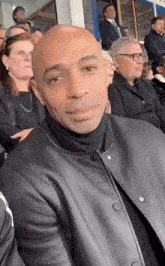 a man in a black leather jacket is sitting in a crowd