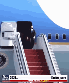 a man walking up the stairs of an airplane with a fox news alert on the bottom right