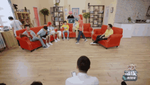 a group of people are sitting on red couches in a living room with a sign that says ' a ' on it