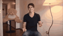 a man in a black shirt is sitting next to a teddy bear .