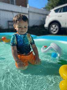 a little boy is kneeling in a swimming pool with a car in the background