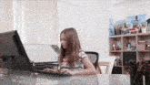 a young girl is sitting at a desk using a computer