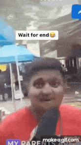a man in a red shirt is talking into a microphone with the words wait for end above him