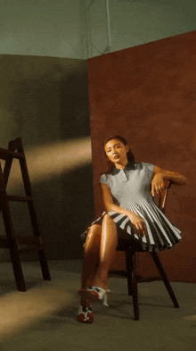 a woman in a striped dress is sitting on a chair with her legs crossed