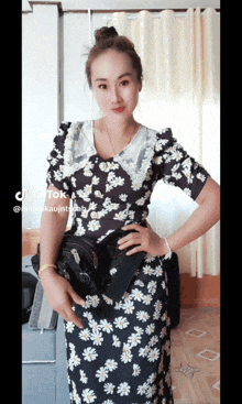 a woman in a black and white floral dress holds a black purse in her hand