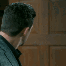 a man in a suit and black shirt is standing in front of a door .