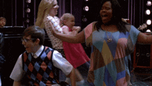 a group of people are dancing in a room and one of them is wearing a plaid vest
