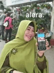 a woman in a green hijab is holding a cell phone in front of a flower shop .