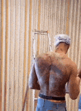 a shirtless man with tattoos on his back is standing in front of a wooden wall .