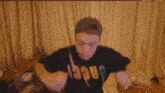 a man in a black t-shirt is standing in front of a window in a living room .