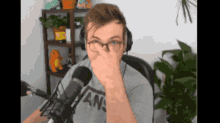 a man wearing glasses and a vans shirt is covering his nose in front of a microphone