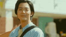 a man wearing a blue and white striped shirt and a black shoulder strap smiles