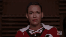 a woman in a cheerleading uniform is making a funny face while sitting in a chair .