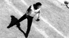 a man in a white tank top and black pants is standing on a dirt field .