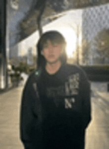 a young man wearing a black hoodie is standing in front of a building .