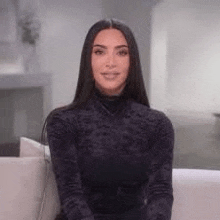a woman is sitting on a couch wearing a black turtleneck sweater and smiling .