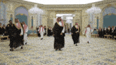 a group of men are dancing in a room with chandeliers