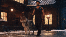 a man walking a wolf down a snowy street in front of a building