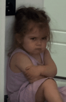 a little girl with her arms crossed is sitting on the floor