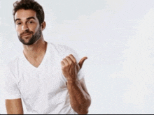 a man with a beard wearing a white t-shirt is giving a thumbs up