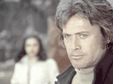 a man with a serious look on his face stands in front of a woman