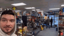 a man wearing a white hoodie is standing in a store filled with lots of toys .