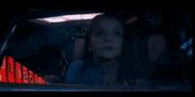 a woman is sitting in a car looking out the window at night .