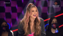 a woman with pink hair is laughing in front of a masterchef sign