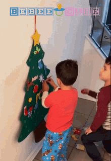 two young boys decorate a christmas tree on a wall with a baby care logo in the corner