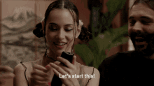 a woman is smiling while holding a cell phone and says let 's start this