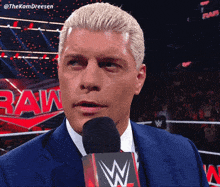 a man in a suit is talking into a microphone in front of a raw sign