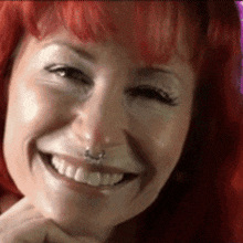 a woman with red hair is smiling with a nose ring in her nose .