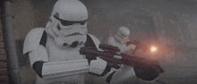 a stormtrooper is holding a gun in his hand while another stormtrooper looks on .