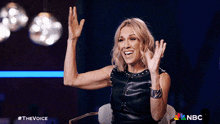 a woman is sitting in a chair with her hands in the air and a nbc logo in the background