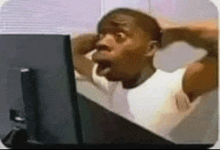 a man is sitting in front of a computer screen with his mouth open and his hands behind his head .
