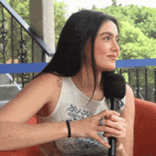 a woman wearing a white tank top with a tattoo on her shoulder is holding a microphone