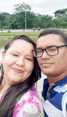 a man and a woman are posing for a picture in front of a lake