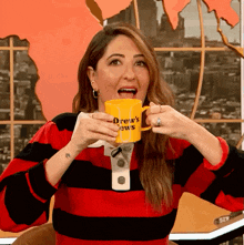 a woman holding a yellow mug that says drew 's news on it