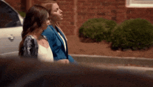 two women standing next to each other in front of a car